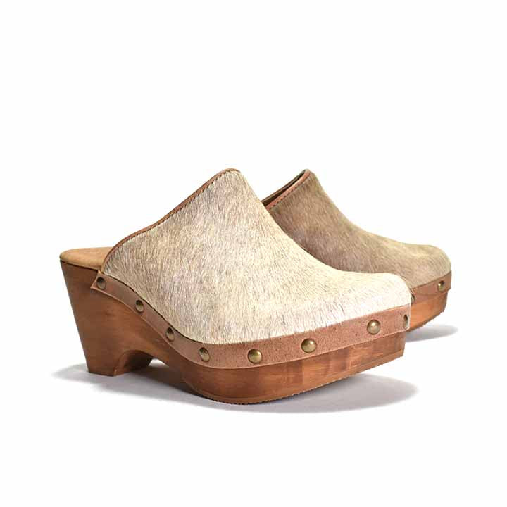 pair of beige cowhair clogs with a light wooden heel, featuring metal eyelets 