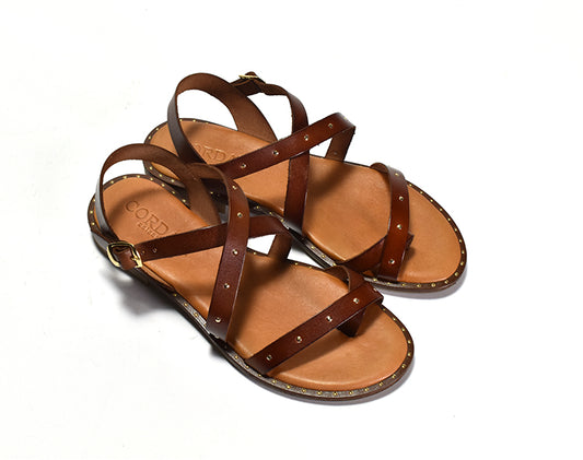 A pair of brown faux leather sandals with a crisscross toe ring design and gold stud details